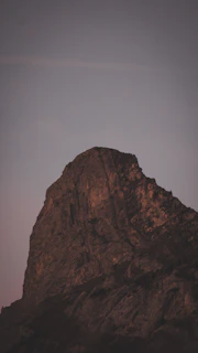 A rugged mountain peak silhouetted against a natural blue sky at dusk, emphasizing the minimalist dark tones.