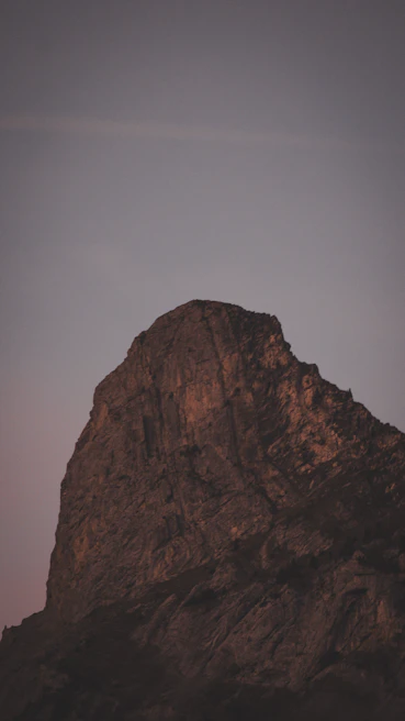 A rugged mountain peak silhouetted against a natural blue sky at dusk, emphasizing the minimalist dark tones.