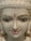 A close-up of a serene white marble statue with intricate facial features. The statue's eyes are delicately painted, and it has a small red symbol on the forehead. The lips are painted a soft pink, and the eyebrows are accentuated with golden highlights.