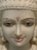 A close-up of a serene white marble statue with intricate facial features. The statue's eyes are delicately painted, and it has a small red symbol on the forehead. The lips are painted a soft pink, and the eyebrows are accentuated with golden highlights.