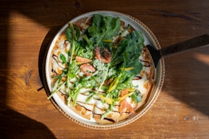 A sprouted wheat pizza topped with fresh vegetables on a rustic wooden table under soft natural light