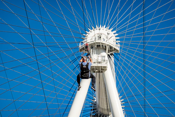 Worker in climbing gear painting a tall steel structure on a sunny day