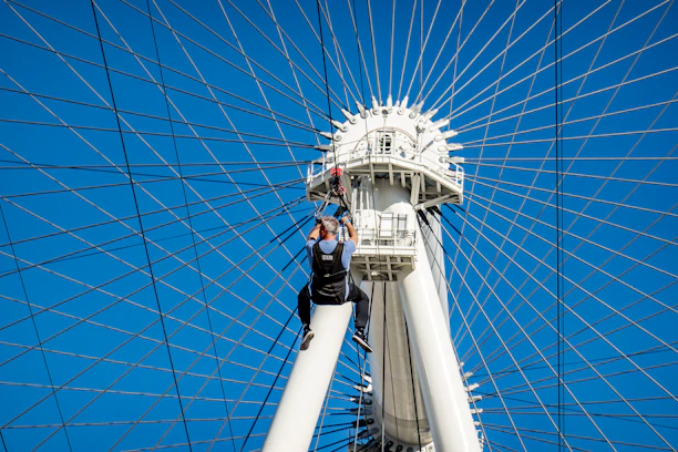 Worker in climbing gear painting a tall steel structure on a sunny day