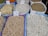 Various types of legumes and grains are displayed in bags at a market. Each bag is marked with a handwritten price sign. The bags include beans, lentils, and chickpeas, among others.