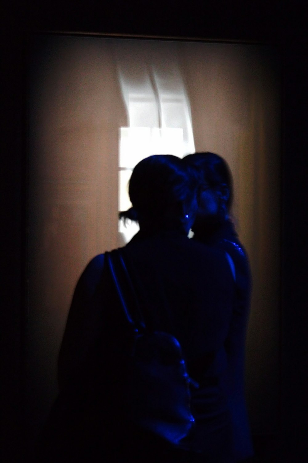 una mujer parada frente a una ventana en la oscuridad
