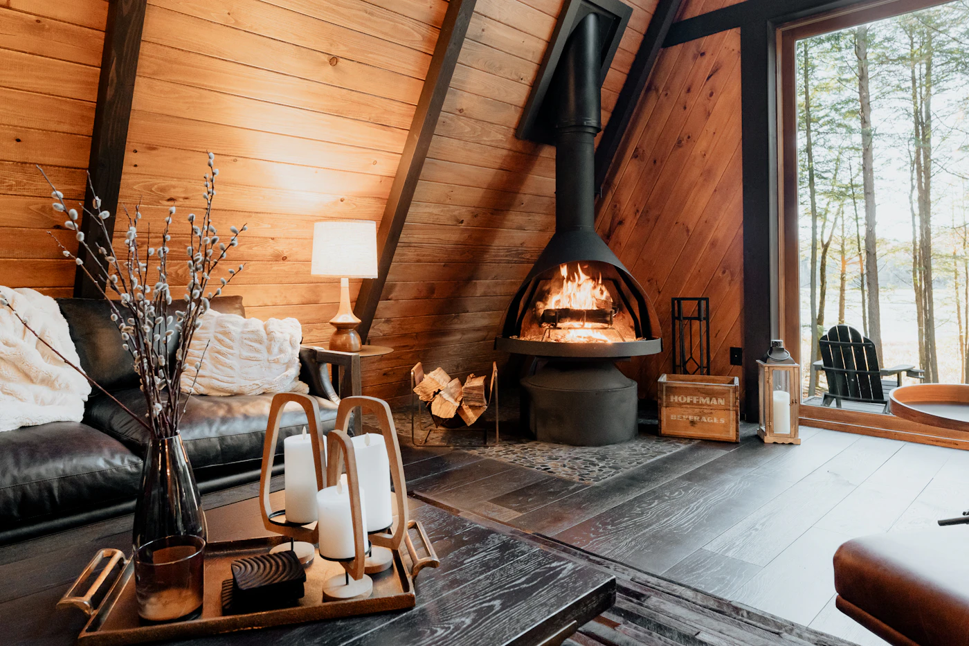 A-frame cabin interior with angled wood ceiling, large windows and wood stove