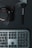 A digital camera with the brand name partially visible, a makeup brush, and a keyboard are arranged on a dark surface with intersecting lines. The camera is on the left, the brush on the right, and the keyboard below.