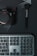 A digital camera with the brand name partially visible, a makeup brush, and a keyboard are arranged on a dark surface with intersecting lines. The camera is on the left, the brush on the right, and the keyboard below.