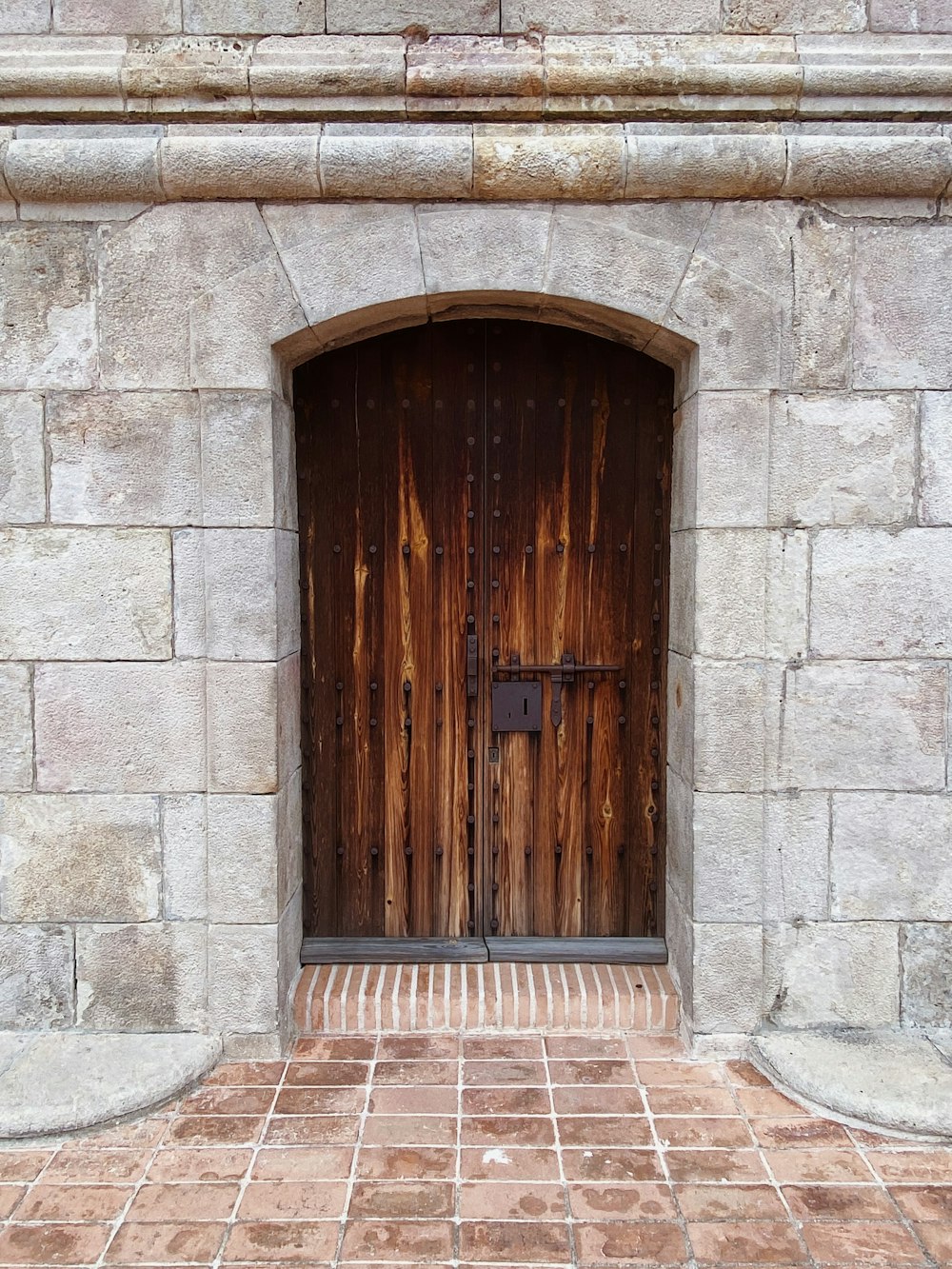 a stone building with two wooden doors and a brick walkway