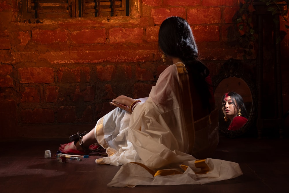 a woman sitting on the floor next to a brick wall