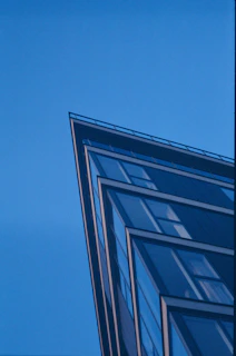 An urban office building with sharp angles and a reflective glass facade under a clear blue sky.