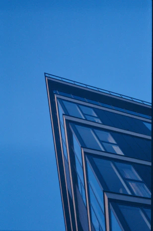 An urban office building with sharp angles and a reflective glass facade under a clear blue sky.