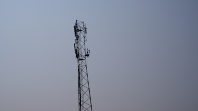A team installing a tall telecommunications tower against a clear blue sky.