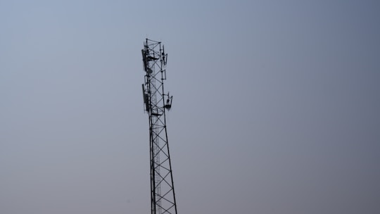 A tall metal telecommunications tower stands against a clear blue sky. The tower features multiple antennas attached along its sides, indicating its use for communication purposes.