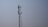 A tall metal telecommunications tower stands against a clear blue sky. The tower features multiple antennas attached along its sides, indicating its use for communication purposes.