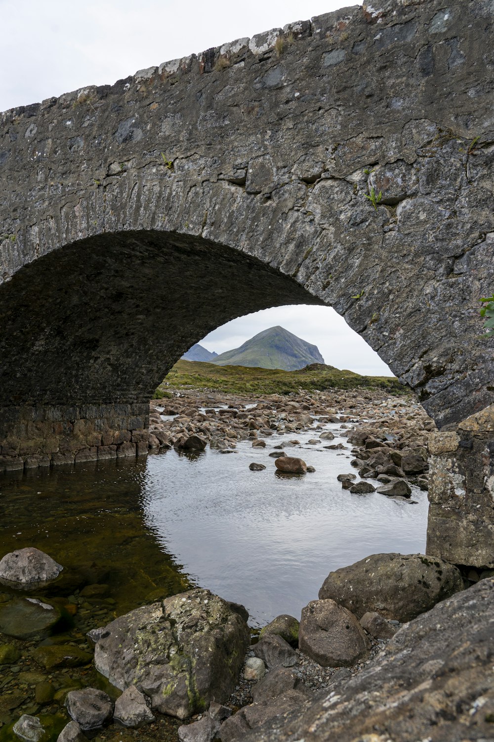 a stone bridge over a river with a mountain in the background