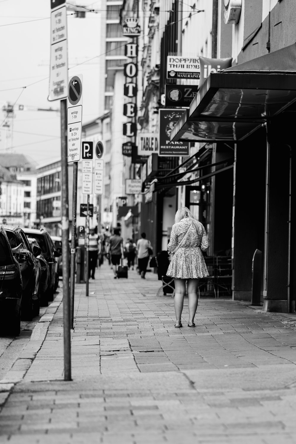 a woman walking down a street next to parked cars