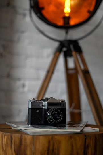 A vintage camera resting on a wooden table surrounded by a spread of black and white and color photographs.