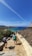 A small group hiking along a rugged coastal trail with turquoise sea views under a clear sky.