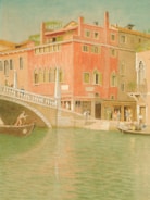 A watercolor painting depicting a canal scene with a vibrant red building featuring arched windows. Two people are visible on gondolas navigating the calm water. The bridge connects to the building, with pedestrians walking along the path.
