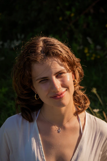 A young woman smiling while wearing minimalist hoop earrings and a casual linen shirt outdoors