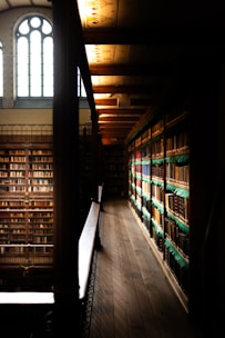 A shadowy library corner illuminated by a flickering golden candle, with ancient books stacked high.