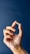 A hand with fingers gracefully holding a small capsule against a solid dark blue background. The skin's texture is visible, highlighting a sense of realism and focus.
