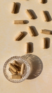 Close-up of Purimea capsules spilling gently from a glass jar onto a wooden surface, bathed in soft natural light.