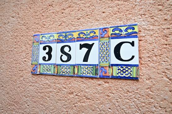 A decorative ceramic tile display with a number '387C' set against a textured terracotta-colored wall. Each tile features ornate patterns with blue, yellow, and red colors.