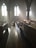 Sunlight streams through the tall, arched windows of an empty church, casting long shadows across the wooden pews and creating an ethereal glow. The atmosphere is calm and serene, enhanced by the soft haze of light.