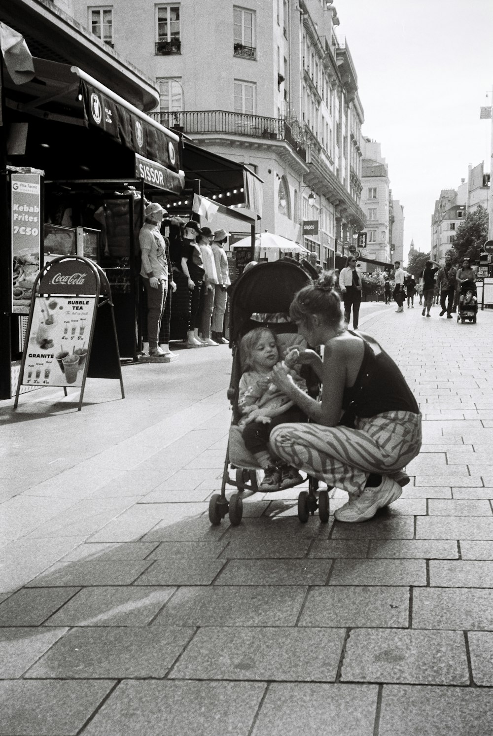 a woman kneeling down next to a baby in a stroller
