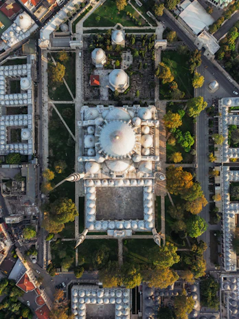 Aerial view of a mosque complex surrounded by lush greenery under a clear blue sky.
