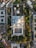 An aerial view of a large mosque complex with multiple domes and courtyards, surrounded by green gardens and trees. The architecture is detailed with symmetrical designs and tall minarets. The surrounding area includes urban buildings and roads.