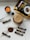 A neatly arranged setup featuring a candle, a large packet of 'Black Gold' coffee, several smaller sticks of instant coffee, a cup of frothy coffee, a black spoon, and a swirl of coffee powder on a light marble surface.