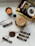 A neatly arranged setup featuring a candle, a large packet of 'Black Gold' coffee, several smaller sticks of instant coffee, a cup of frothy coffee, a black spoon, and a swirl of coffee powder on a light marble surface.