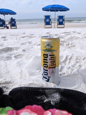 Caribe Cooler bottles arranged on a beach towel with ocean waves in the background.