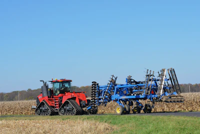 A powerful red agricultural tractor working in a golden wheat field under a clear blue sky.