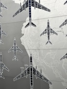Illustrations of several airplanes are overlaid on a map-like background, with contour lines suggesting topographical features. The airplanes are drawn in a technical, blueprint style, and are arranged in various orientations across the image.
