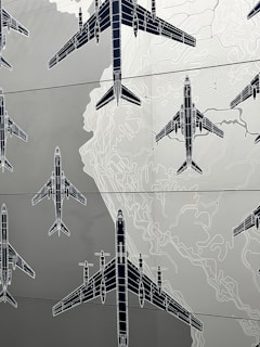 Illustrations of several airplanes are overlaid on a map-like background, with contour lines suggesting topographical features. The airplanes are drawn in a technical, blueprint style, and are arranged in various orientations across the image.