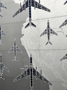 Illustrations of several airplanes are overlaid on a map-like background, with contour lines suggesting topographical features. The airplanes are drawn in a technical, blueprint style, and are arranged in various orientations across the image.
