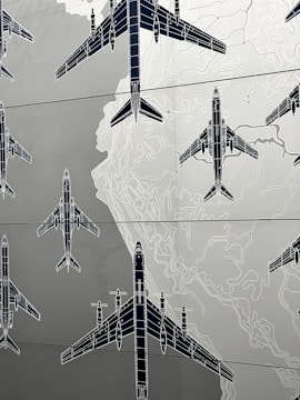 Illustrations of several airplanes are overlaid on a map-like background, with contour lines suggesting topographical features. The airplanes are drawn in a technical, blueprint style, and are arranged in various orientations across the image.