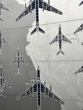 Illustrations of several airplanes are overlaid on a map-like background, with contour lines suggesting topographical features. The airplanes are drawn in a technical, blueprint style, and are arranged in various orientations across the image.