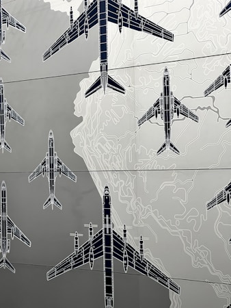 Illustrations of several airplanes are overlaid on a map-like background, with contour lines suggesting topographical features. The airplanes are drawn in a technical, blueprint style, and are arranged in various orientations across the image.