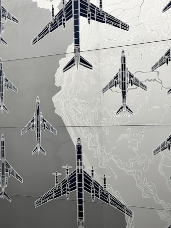 Illustrations of several airplanes are overlaid on a map-like background, with contour lines suggesting topographical features. The airplanes are drawn in a technical, blueprint style, and are arranged in various orientations across the image.