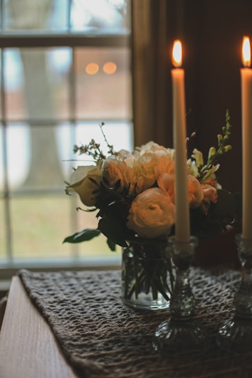 A bouquet of fresh flowers with candles on a wooden table.