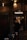 A person is standing in front of a ticket booth labeled 'TAQUILLA' with a light overhead. The setting is dimly lit, with brick walls and string lights providing a warm ambiance. The person appears to be handling a phone or device.