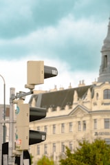 A traffic light with visible countdown timers displaying the numbers 15 and 9, set against a backdrop of a historic, ornate building with a pointed tower. The sky is cloudy, adding a moody atmosphere.