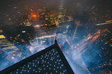 Nighttime city skyline viewed from a rooftop lounge, featuring muted gold lighting and a male influencer looking out.