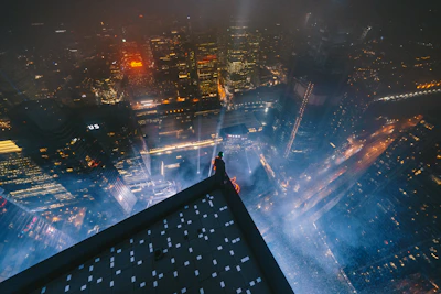 Nighttime city skyline viewed from a rooftop lounge, featuring muted gold lighting and a male influencer looking out.