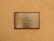 A metallic plaque with a wooden frame mounted on a textured beige wall. The plaque has the text 'The Luxury Collection' engraved in black, centered on its surface.